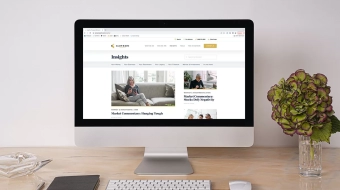 Mac desktop computer on a clean desk with some flowers, screen displays Carson Wealth Insights Blog webpage